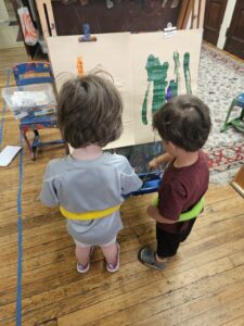 Two young children are painting at an easel.