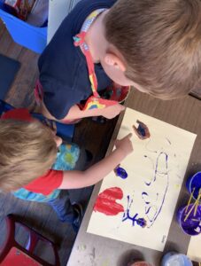 Two young boys are painting with paint on a paper.