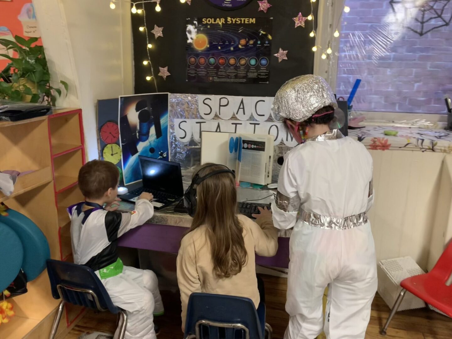 Three children in costumes work at a constructed space station.